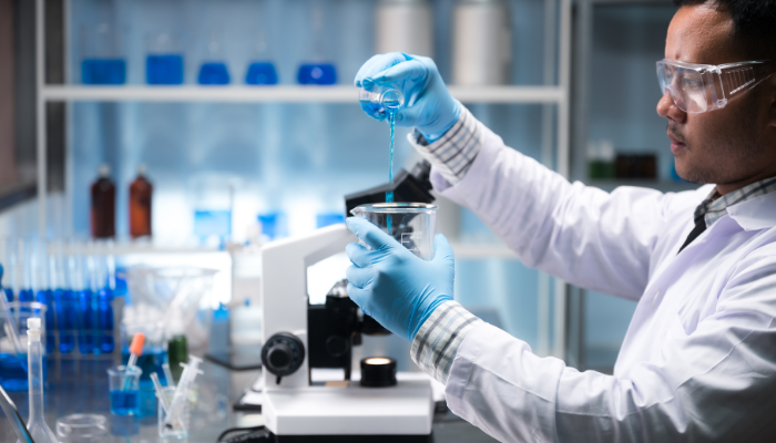 En forskare häller blå vätska i en bägare i ett laboratorium
