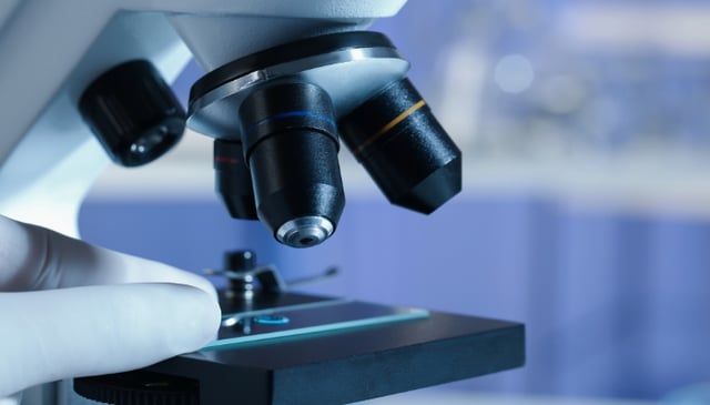 Close-up of a gloved hand placing a slide under a laboratory microscope